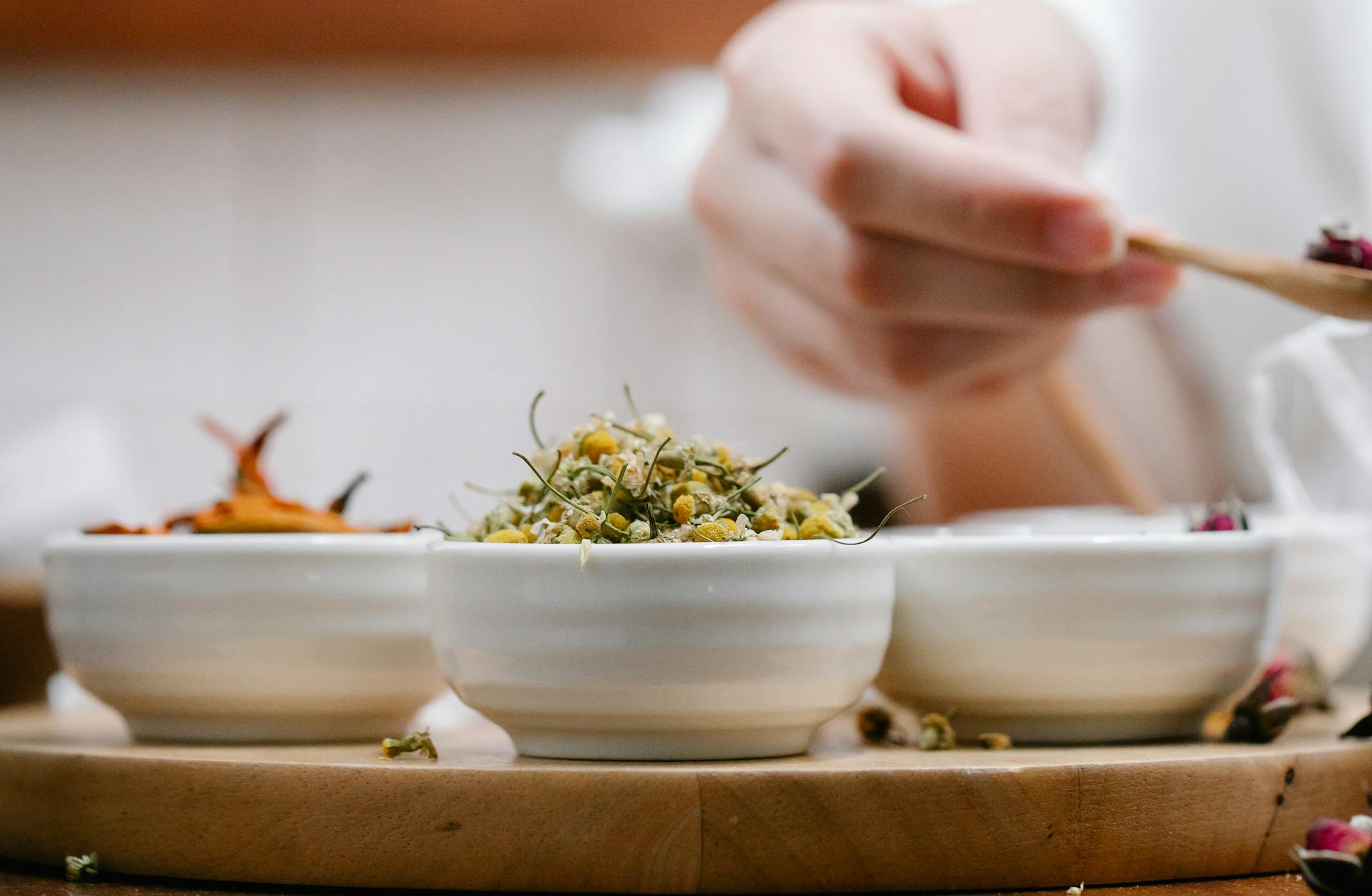 A detailed close-up of hands preparing herbal ingredients in ceramic bowls, highlighting natural aromas.