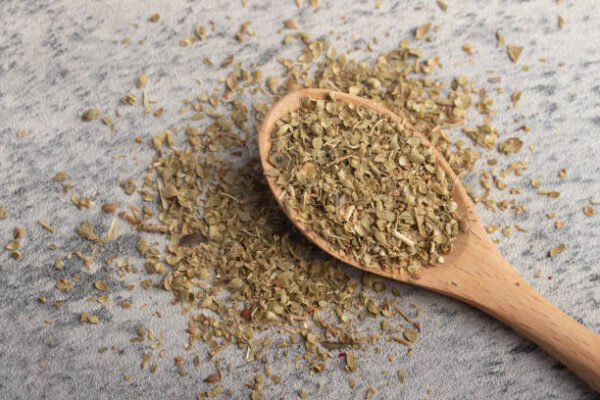 Oregano in wooden spoon on gray background
