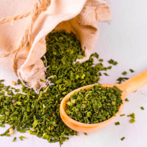 Baggy sack with dried green spices and a wooden spoon on a white kitchen table