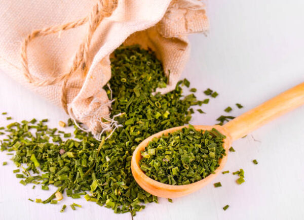 Baggy sack with dried green spices and a wooden spoon on a white kitchen table